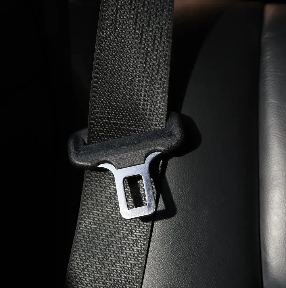 Seat belt webbing and metal latch plate photographed against a dark vehicle interior