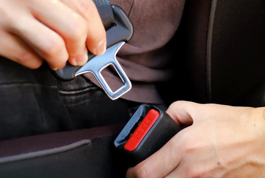 Hands bringing a seat belt latch plate and buckle receiver together between vehicle seats