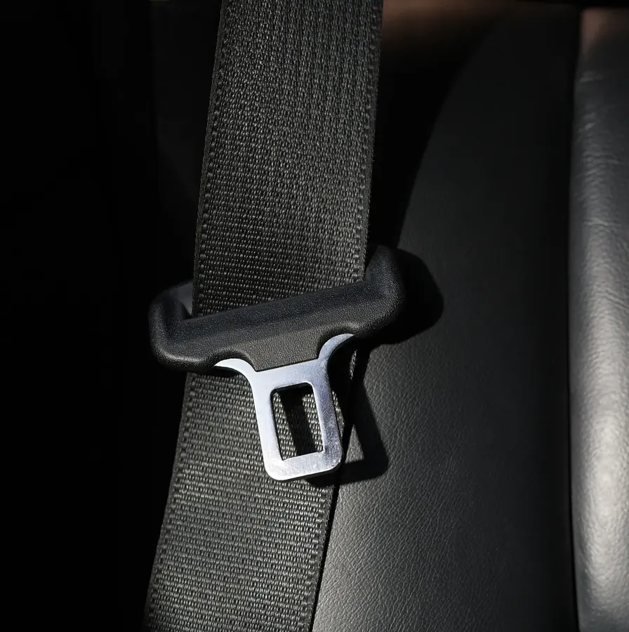 Seat belt webbing and metal latch plate photographed against a dark vehicle interior