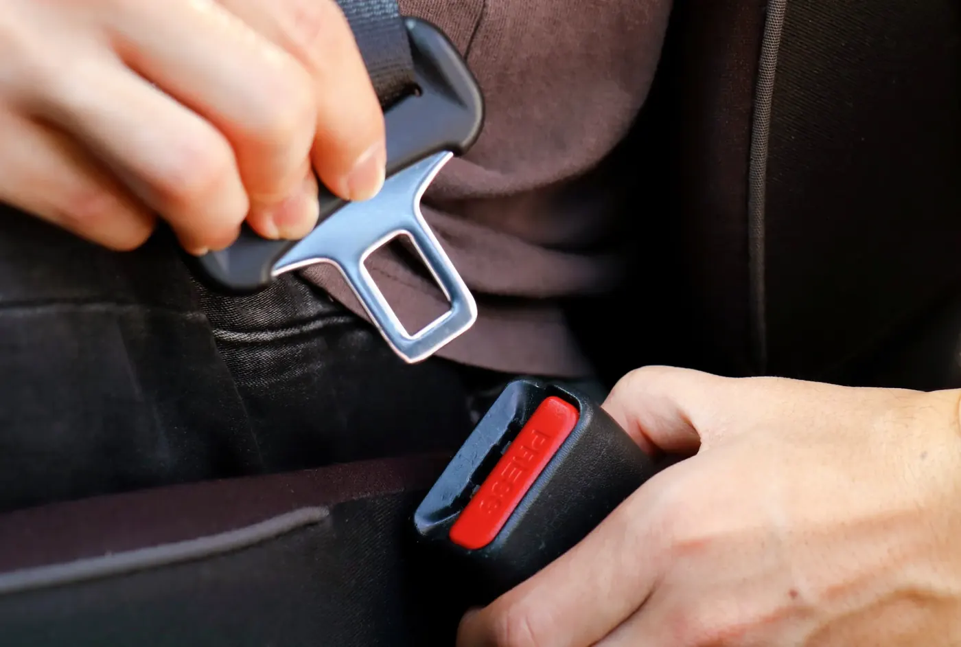 Hands guiding a seat belt latch plate towards the buckle receiver between two vehicle seats