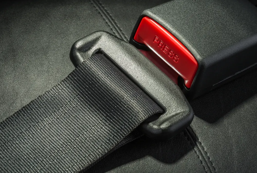 Seat belt webbing, latch plate and buckle receiver photographed on a dark leather seat