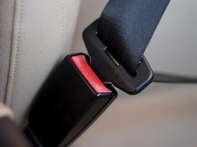 Seat belt tongue being guided towards a black buckle receiver inside a light coloured car interior