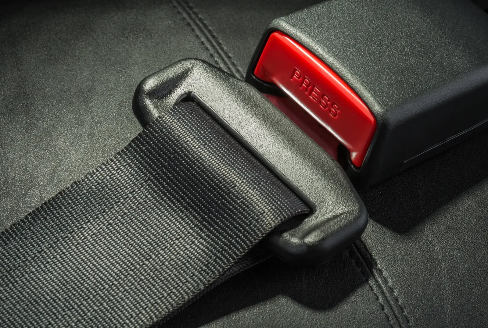 Macro photograph of seat belt webbing, a black latch plate and a red release button on the buckle receiver