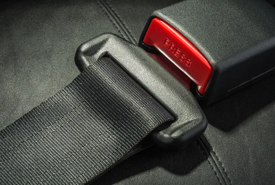 Seat belt webbing, latch plate and buckle receiver photographed on a dark leather seat