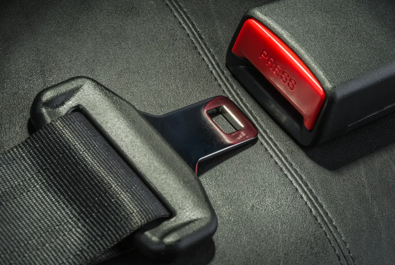 Seat belt latch plate and buckle receiver photographed on a dark leather vehicle seat