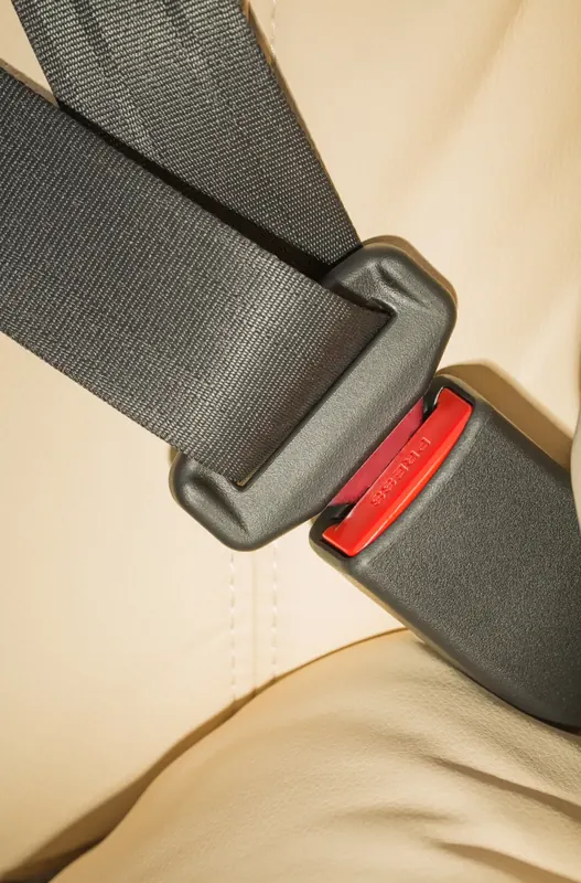 Seat belt webbing entering a buckle with a red release on a cream leather seat